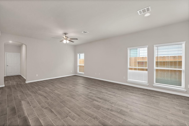unfurnished room with visible vents, a ceiling fan, baseboards, dark wood-style floors, and arched walkways