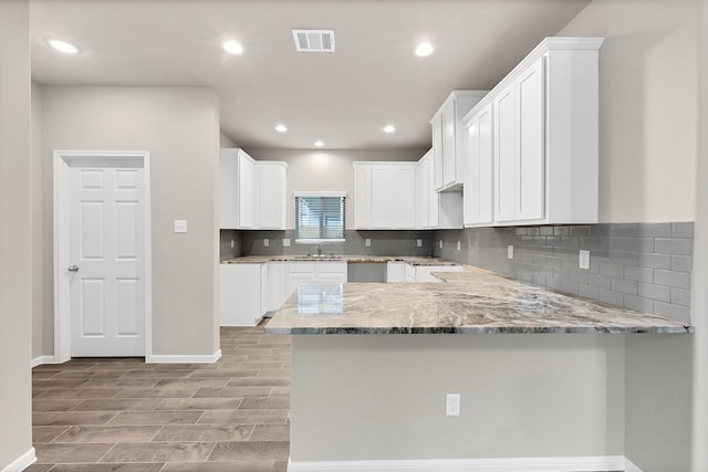 kitchen with light stone countertops, a peninsula, baseboards, tasteful backsplash, and visible vents