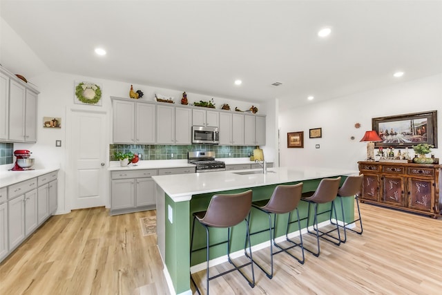 kitchen with gray cabinetry, appliances with stainless steel finishes, a kitchen breakfast bar, and backsplash