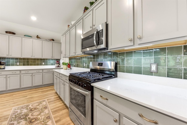 kitchen featuring backsplash, light wood-type flooring, light countertops, gray cabinetry, and stainless steel appliances