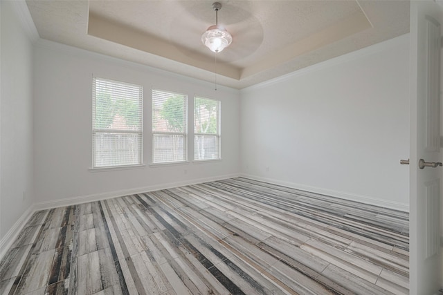 empty room with baseboards, a ceiling fan, a raised ceiling, and wood finished floors
