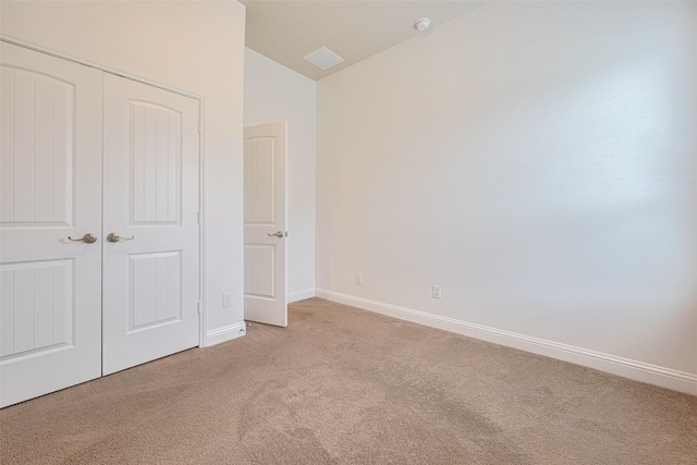 unfurnished bedroom featuring visible vents, a closet, lofted ceiling, baseboards, and light colored carpet