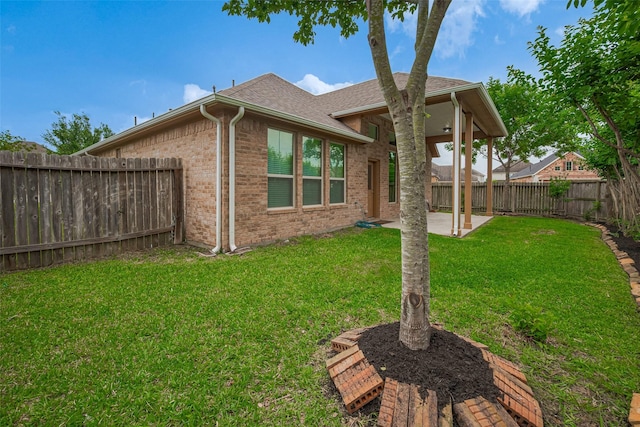 rear view of house with roof with shingles, a lawn, a patio area, brick siding, and a fenced backyard