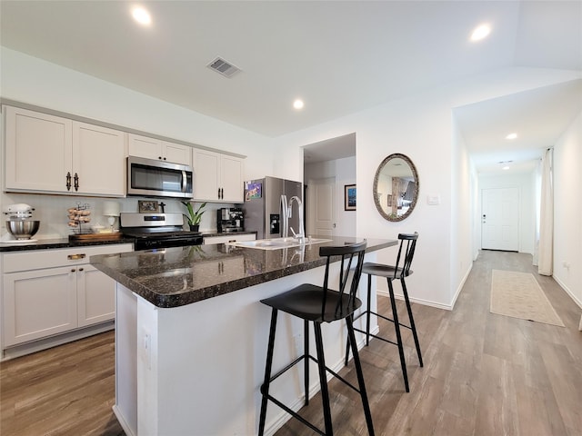 kitchen with visible vents, a breakfast bar, an island with sink, a sink, and appliances with stainless steel finishes