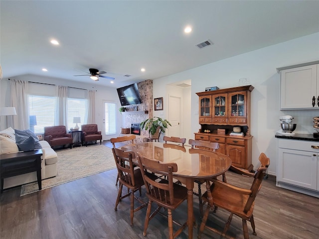 dining space with ceiling fan, dark wood finished floors, a stone fireplace, and visible vents