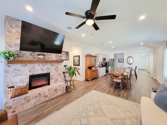 living area featuring ceiling fan, a fireplace, light wood-style floors, baseboards, and visible vents