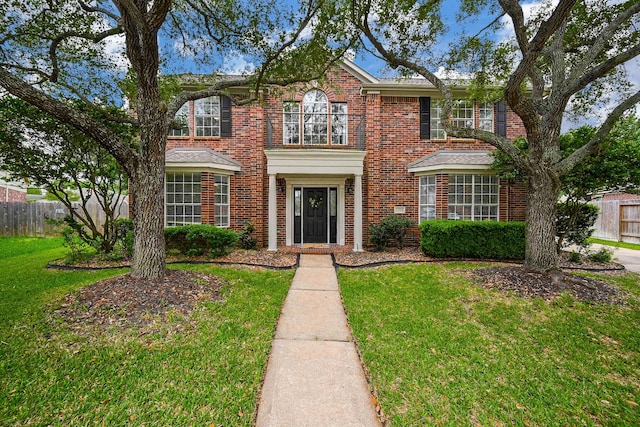 colonial-style house with brick siding, fence, and a front yard