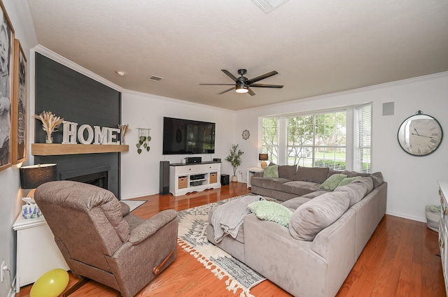 living area featuring crown molding, ceiling fan, a fireplace, baseboards, and wood finished floors