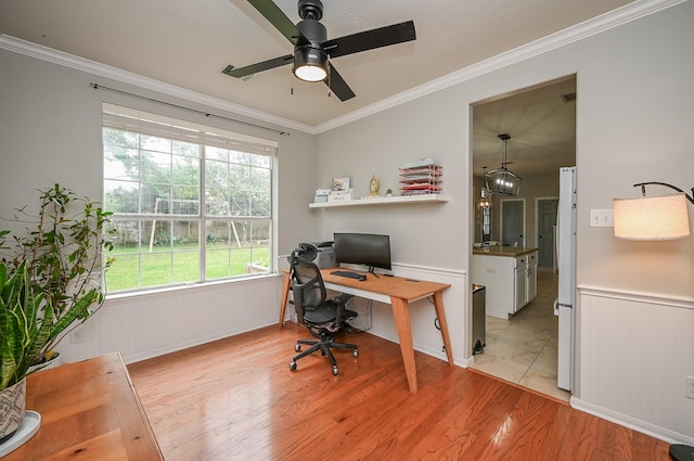 home office featuring light wood-style floors, ornamental molding, wainscoting, and a ceiling fan