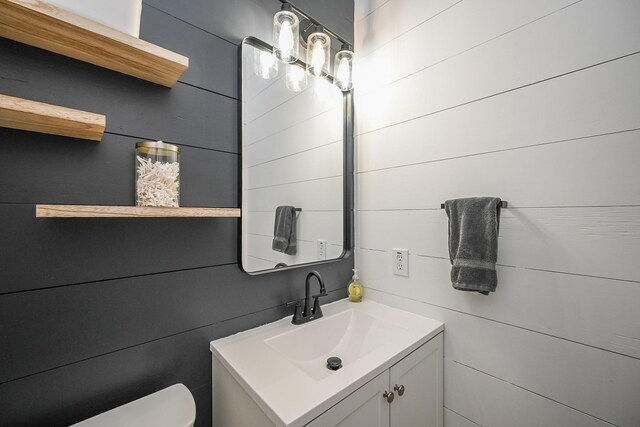 bathroom with vanity, wood walls, and toilet