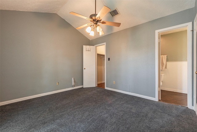 unfurnished bedroom featuring visible vents, lofted ceiling, baseboards, dark colored carpet, and a spacious closet