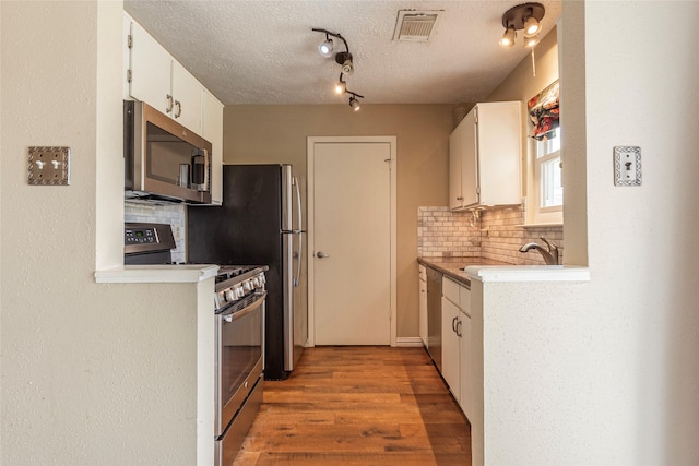 kitchen featuring a textured ceiling, visible vents, appliances with stainless steel finishes, tasteful backsplash, and light wood finished floors