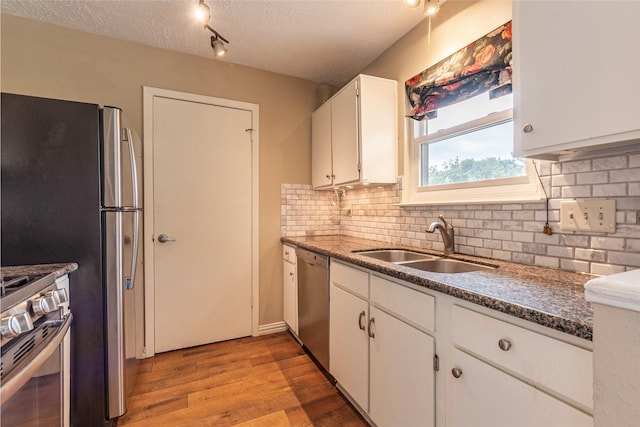 kitchen with decorative backsplash, appliances with stainless steel finishes, a sink, light wood-style floors, and white cabinetry