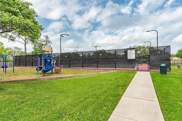view of tennis court with a yard, fence, and playground community