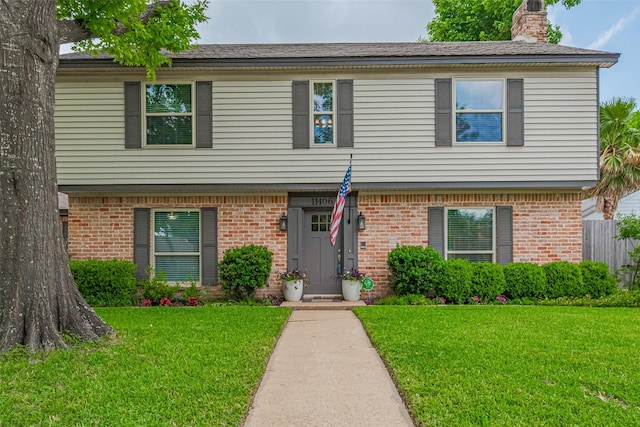 view of front of house with a chimney, brick siding, and a front yard