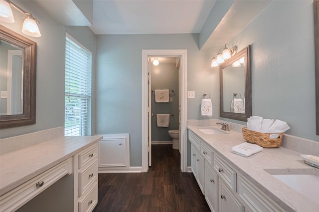 full bathroom with a sink, double vanity, toilet, and wood finished floors