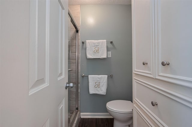 full bath featuring baseboards, a shower stall, toilet, and wood finished floors