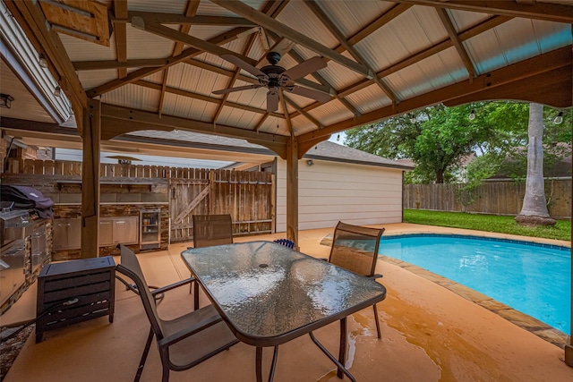 view of pool with a ceiling fan, a gazebo, a fenced in pool, a fenced backyard, and an outdoor kitchen