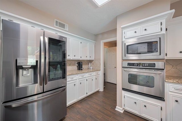 kitchen with backsplash, visible vents, dark wood finished floors, stainless steel appliances, and white cabinetry