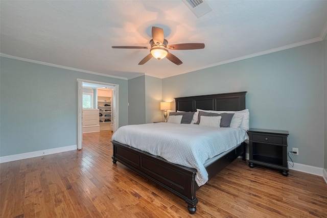 bedroom featuring a ceiling fan, visible vents, wood finished floors, baseboards, and ornamental molding