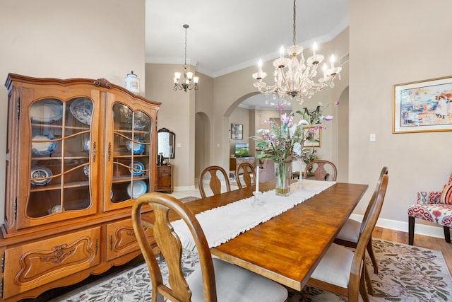 dining room with ornamental molding, wood finished floors, baseboards, arched walkways, and a notable chandelier