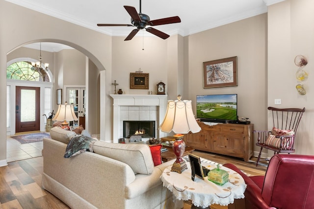 living area with ornamental molding, wood finished floors, ceiling fan, a tiled fireplace, and arched walkways