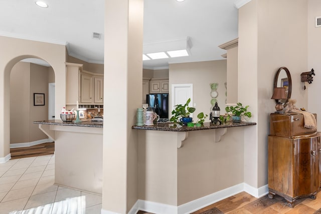 kitchen with dark stone counters, cream cabinets, freestanding refrigerator, and visible vents