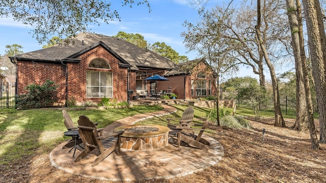 rear view of property featuring roof with shingles, fence, brick siding, a patio, and a fire pit