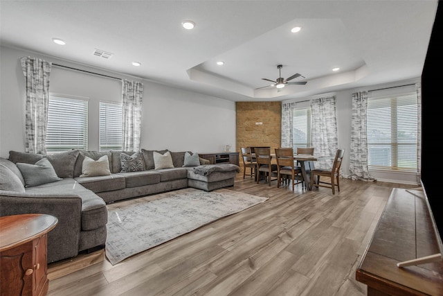 living area featuring light wood finished floors, a raised ceiling, a ceiling fan, recessed lighting, and visible vents