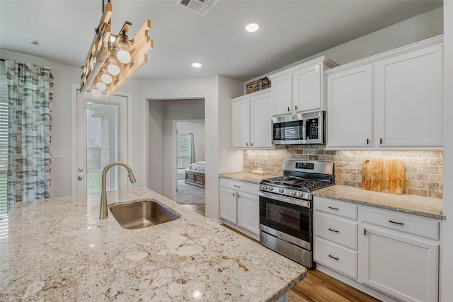 kitchen with white cabinets, appliances with stainless steel finishes, a sink, backsplash, and visible vents