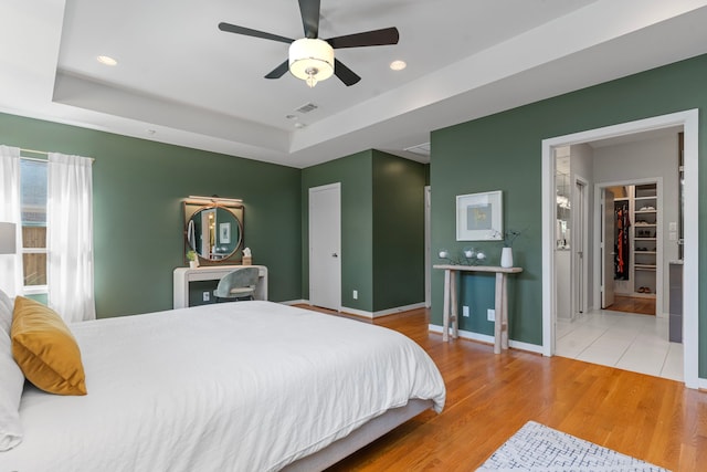 bedroom with baseboards, a tray ceiling, wood finished floors, and visible vents