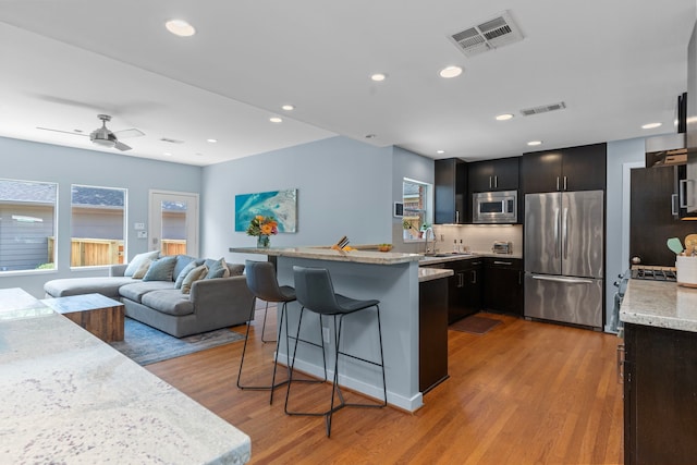 kitchen featuring a kitchen breakfast bar, stainless steel appliances, light wood finished floors, and visible vents
