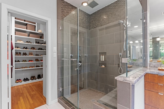 full bathroom featuring a walk in closet, visible vents, wood finished floors, and a stall shower