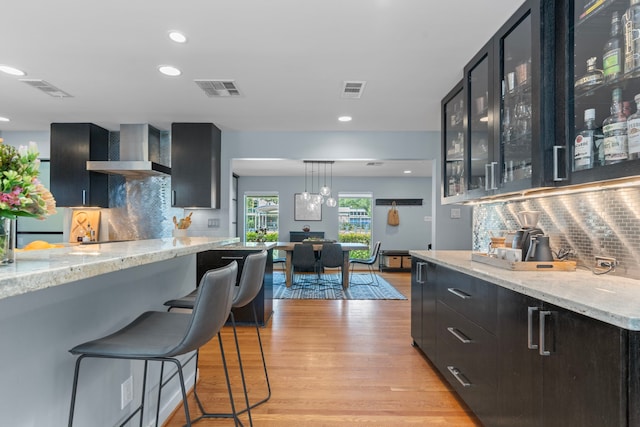 kitchen featuring light wood-style floors, decorative backsplash, wall chimney exhaust hood, and visible vents