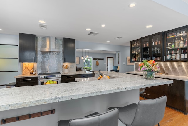 kitchen with visible vents, wall chimney exhaust hood, a breakfast bar area, and stainless steel gas range