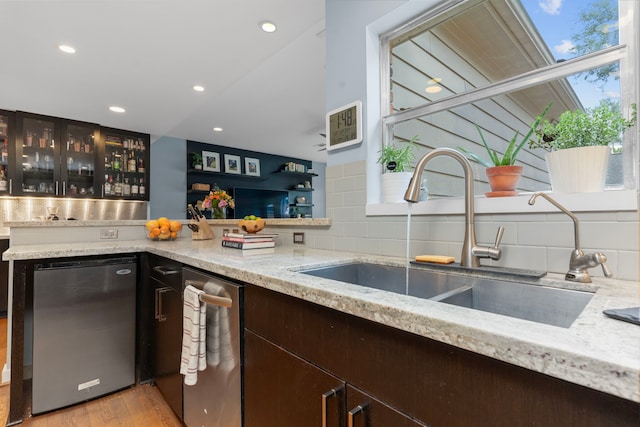 kitchen featuring dark brown cabinetry, a sink, light wood-style floors, recessed lighting, and glass insert cabinets