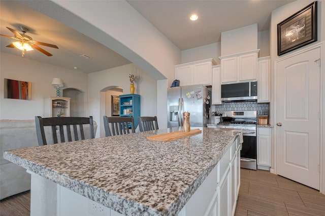 kitchen with decorative backsplash, a kitchen island, appliances with stainless steel finishes, arched walkways, and white cabinets