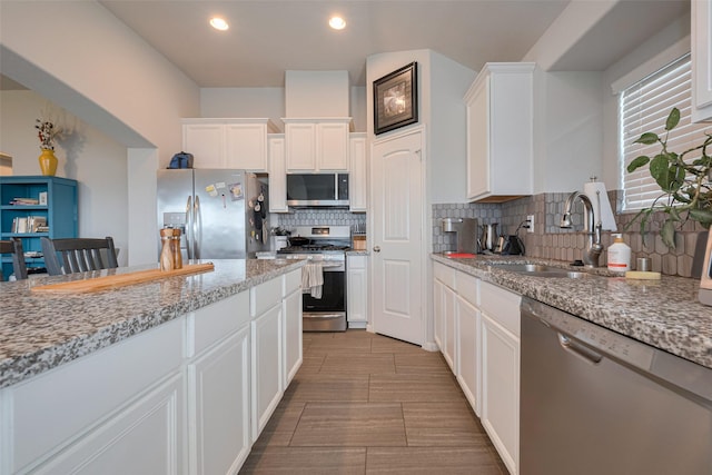 kitchen featuring light stone countertops, appliances with stainless steel finishes, a sink, white cabinetry, and decorative backsplash