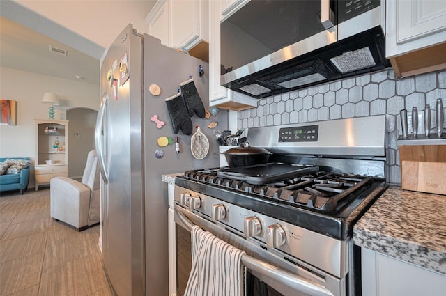 kitchen featuring light stone counters, stainless steel appliances, white cabinetry, backsplash, and visible vents