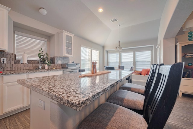 kitchen with a kitchen bar, visible vents, a center island, a sink, and white cabinets