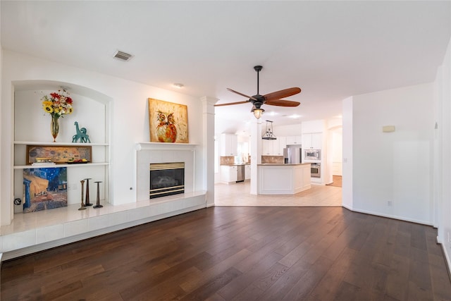 54 N Crossed Birch Pl, The Woodlands, TX 77381 - unfurnished living room featuring visible vents, baseboards, light wood-type flooring, a tiled fireplace, and a ceiling fan