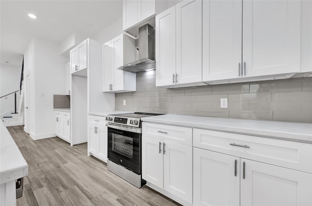 kitchen with wall chimney range hood, stainless steel electric stove, light countertops, white cabinetry, and recessed lighting