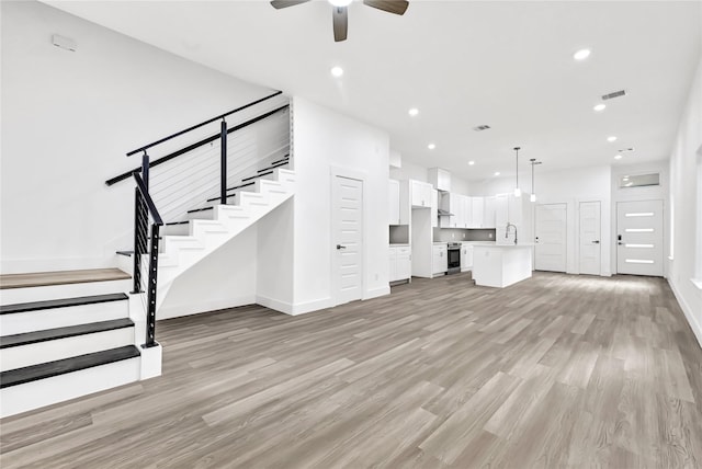 unfurnished living room with light wood-type flooring, a ceiling fan, baseboards, recessed lighting, and stairway
