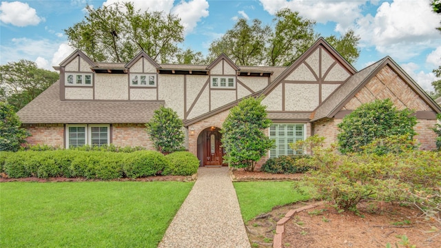 english style home with roof with shingles, a front yard, and stucco siding