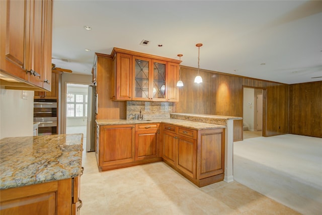 kitchen with brown cabinets, a sink, a peninsula, wooden walls, and stainless steel appliances