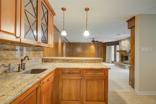 kitchen with brown cabinets, a peninsula, light stone counters, and a sink