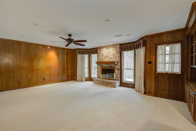 unfurnished living room featuring light carpet, a brick fireplace, wood walls, a ceiling fan, and visible vents