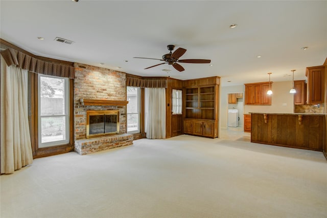 unfurnished living room with a ceiling fan, washer / clothes dryer, visible vents, a brick fireplace, and light carpet
