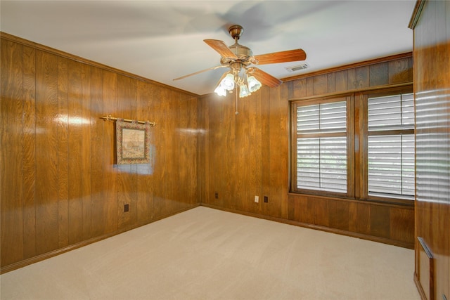 empty room featuring ceiling fan, carpet, wood walls, and visible vents