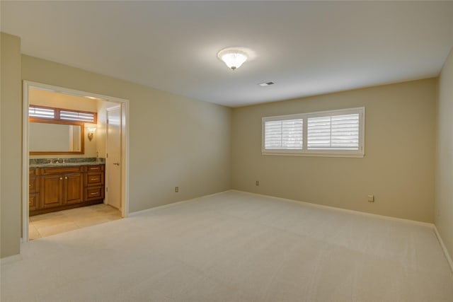 unfurnished bedroom with baseboards, multiple windows, ensuite bath, and light colored carpet